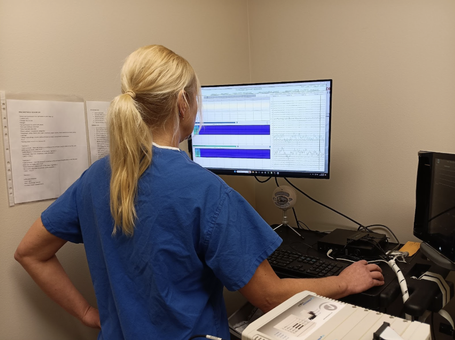 A person in blue scrubs analyzes data on a computer monitor in a medical setting.